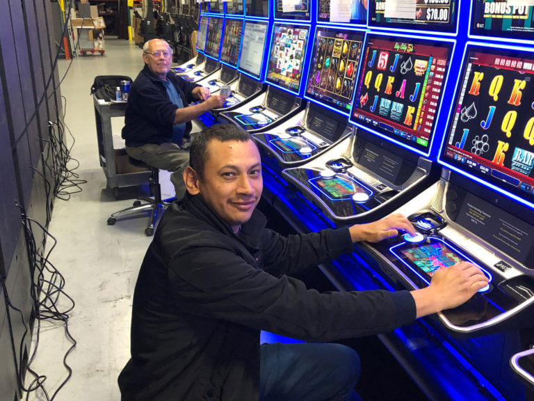 two employees repairing a line of video lottery machines in a warehouse