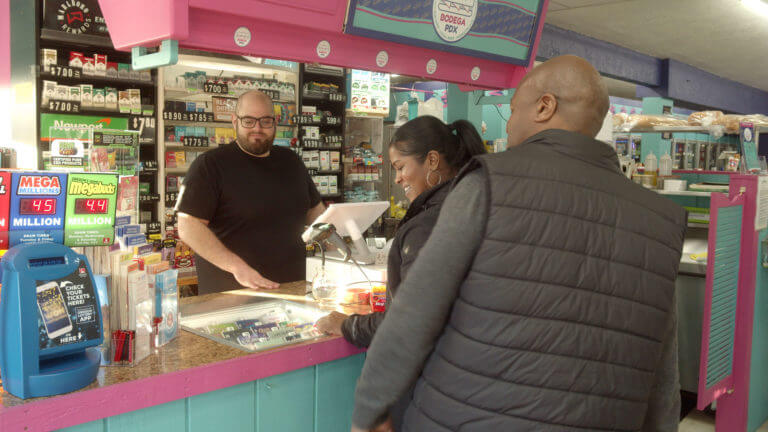 A person at a convenience store counter sells Scratch-its to two people