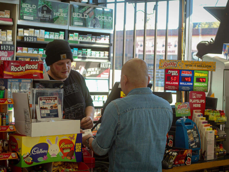 person purchasing Lottery products at convenience store counter, talking to retailer behind the counter