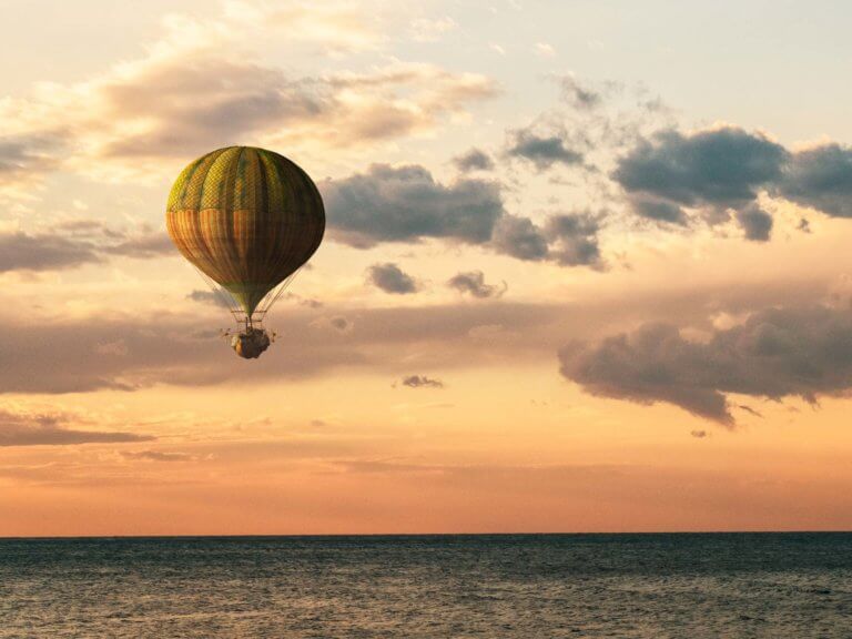 Sunset over the ocean with an old fashioned hot air balloon in the distance
