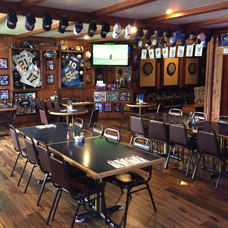 Dining area of sports bar, with lots of sports memorabilia on the walls, tables and chairs in foreground, and dartboards and TV screens in the background