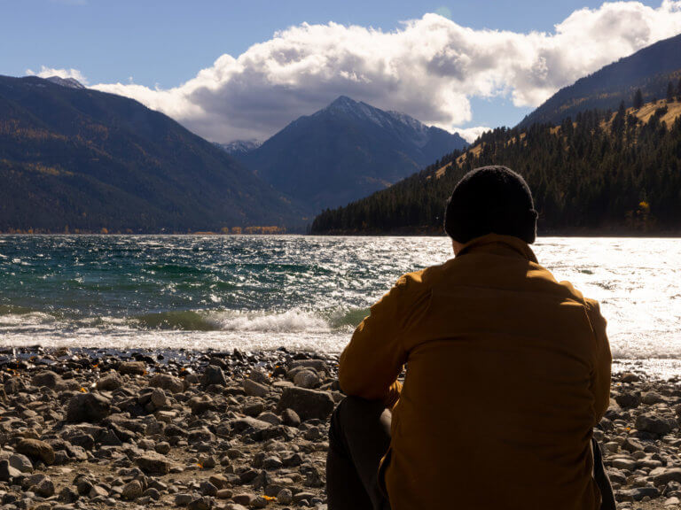 A man sits on shore and contemplates Lake Wallowa