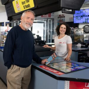 an older gentleman buying scratch-its at a retail counter, smiling at the camera with the cashier