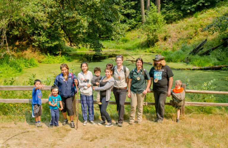 A park ranger posing with a family group in front of a fence