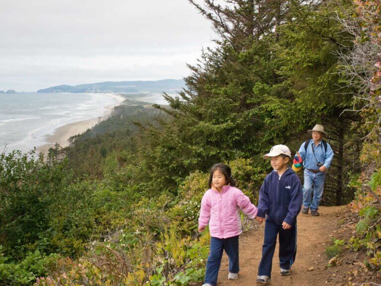 Two children and a man hike on a trail overlooking the ocean