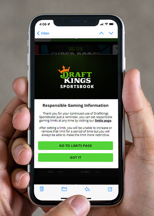 hand holding an iPhone with the DraftKings app opened. On the app is a pop-up message promoting Responsible Gaming practices.