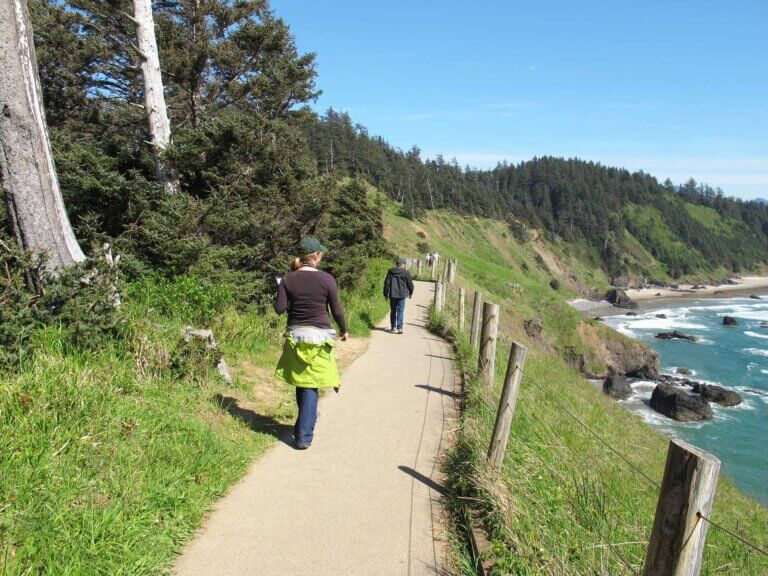 Two people hike away from the camera on a trail overlooking the ocean