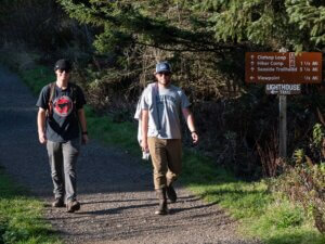Two men hike down a trail next to a trail sign