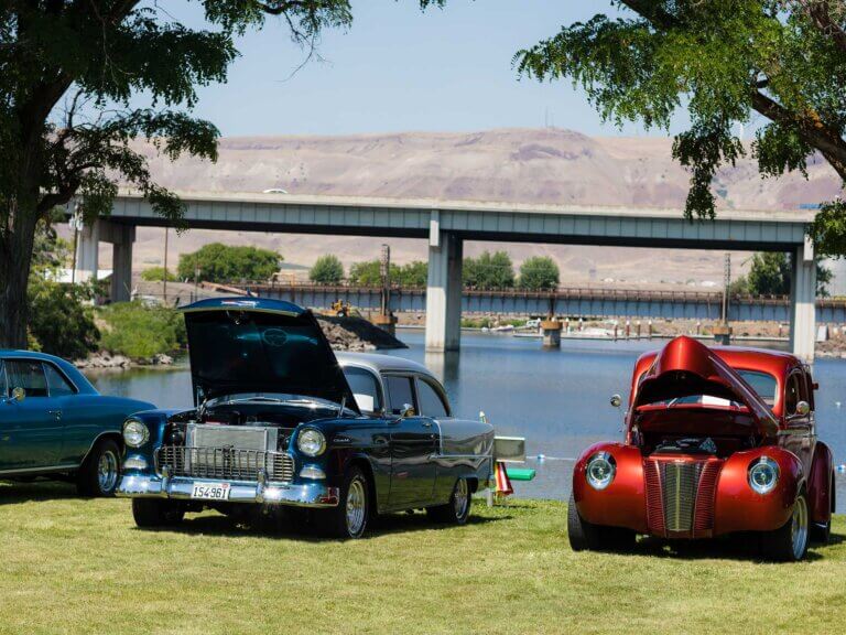 Two cars on display aside a river in a car show.