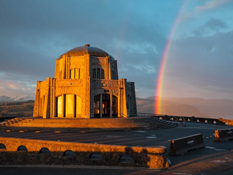 A view of Vista House on Crown Point with a rainbow in the background